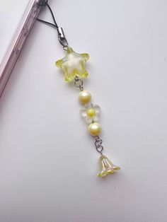 a cell phone charm with yellow and white beads on it's side, attached to a silver chain