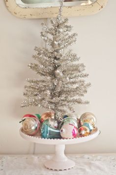 a small silver christmas tree sitting on top of a white cake plate next to a mirror