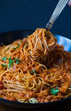 a fork full of spaghetti with tomato sauce and parsley on top, in a skillet