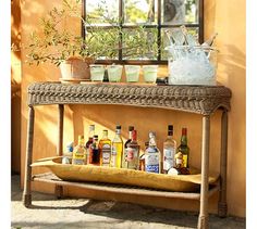 a shelf with bottles and glasses on it next to a potted plant in front of a window