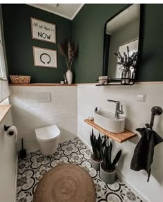 a white toilet sitting next to a sink in a bathroom under a framed mirror above a wooden shelf