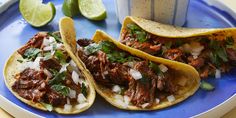 two tacos on a blue plate with limes and a cup in the background