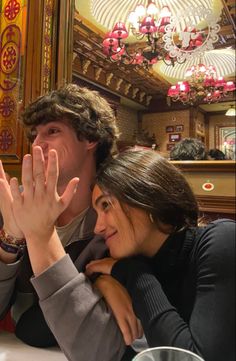 a man and woman sitting at a table with their hands in the air