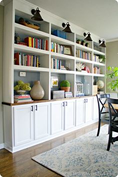 a room filled with lots of white bookshelves next to a dining room table