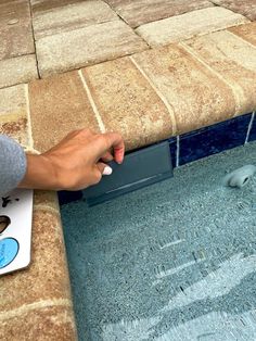 a person with their hand on the edge of a swimming pool near a tile floor