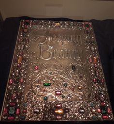 an ornate metal box with beads and stones on the lid is sitting on a black surface