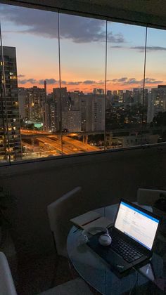 a laptop computer sitting on top of a glass table in front of a large window