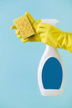 a hand in yellow rubber gloves holding a sponge and detergent on a blue background