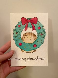 a hand holding up a christmas card with a hedge in a wreath on the front