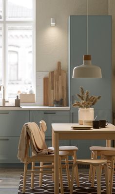 a dining room table and chairs in front of a kitchen with blue cabinets, white walls and windows