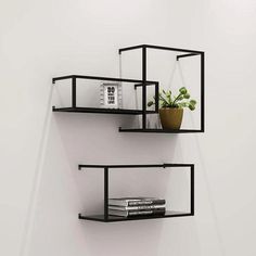 two black shelves with books and plants on them against a white wall next to a potted plant