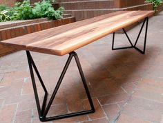 a long wooden bench sitting on top of a brick floor next to some planters