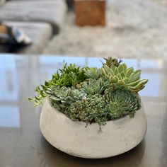 a white vase filled with green plants on top of a table