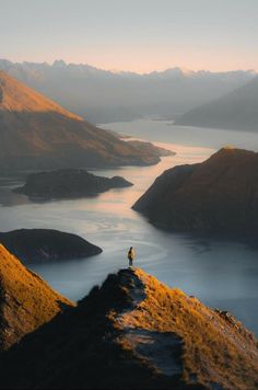 a person standing on top of a mountain overlooking a lake and mountains in the distance