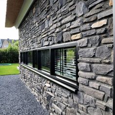 the side of a house made out of stone and black shutters, with grass in the background