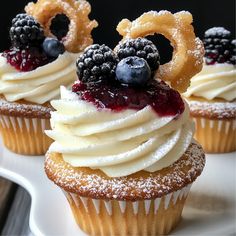 three cupcakes with white frosting and blueberries on top sit on a plate