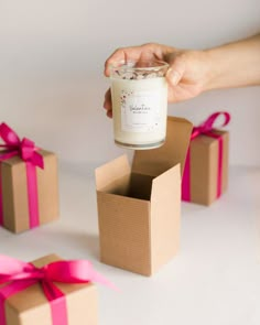 a person holding a candle in a box with pink ribbon around it and other boxes surrounding it