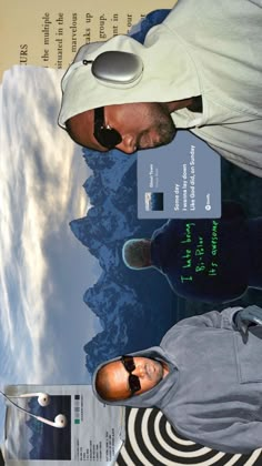 two men standing next to each other in front of a poster with mountains and clouds