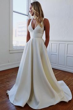 a woman standing in front of a window wearing a white dress with pockets on the side