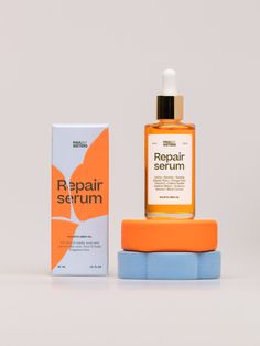 a bottle of repair serum next to a box on a white surface with an orange flower