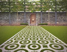 an intricately designed lawn in front of a stone wall and wooden door with grass growing on it