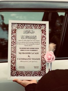 a person holding up a certificate in front of a car with a rose on it