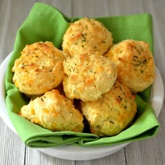 a white bowl filled with cheesy biscuits on top of a green napkin