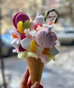 a hand holding an ice cream cone filled with candies and marshmallows