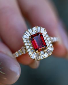 a close up of a person holding a ring with a red stone and white diamonds