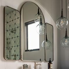 a bathroom sink with two mirrors and lights hanging above it, in front of a window