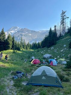 several tents set up on the side of a hill with mountains in the background and trees