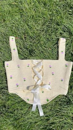 the back of a knitted baby's top with bows on it, laying in grass