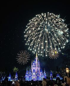 fireworks are lit up in the sky above a castle at disney world with people looking on