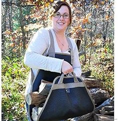 a woman is holding a large bag in the woods with logs and trees behind her