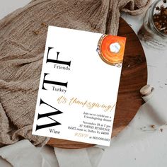 a white and gold thanksgiving party card on top of a wooden plate with an orange candle