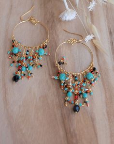 a pair of earrings with beads and chains hanging from them on a wooden table next to flowers