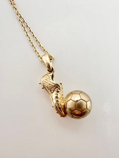 a gold necklace with a soccer ball hanging from it's center and two hands holding the ball