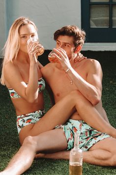 a man and woman sitting on the grass drinking