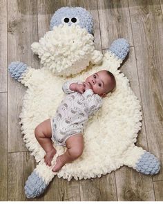 a baby laying on top of a white rug next to a stuffed animal toy in the shape of a sheep