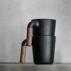 a black cup with a wooden handle on the table next to a gray wall and floor