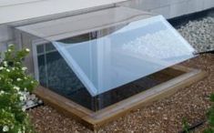 a glass box sitting on top of a gravel ground next to a planter filled with flowers