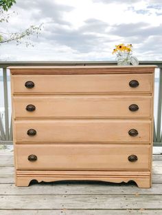 a wooden dresser sitting on top of a wooden floor next to a balcony with flowers in a vase