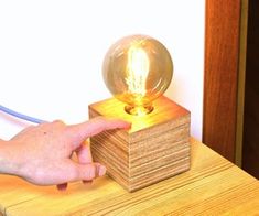 a person is pointing at a light bulb on a wooden block