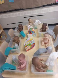 several plastic containers filled with baby dolls sitting on top of a wooden table covered in toys