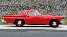 an old red car is parked on the side of the road in front of a stone wall