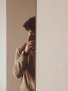 a man standing in front of a white wall holding a cell phone to his face