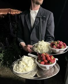 a man in a suit holding three trays of food with strawberries on them