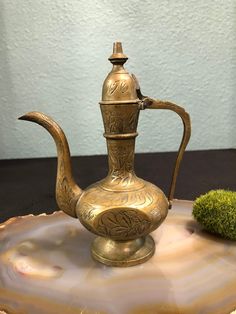 a brass tea pot sitting on top of a marble slab next to a green plant