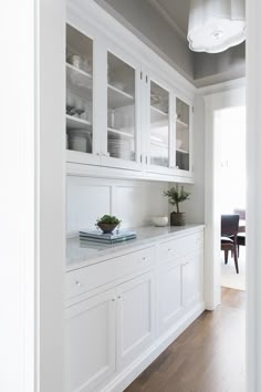 a kitchen with white cabinets and wood flooring next to a dining room table in the background