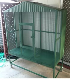 a large green cage sitting in the middle of a floor next to a wall and fence